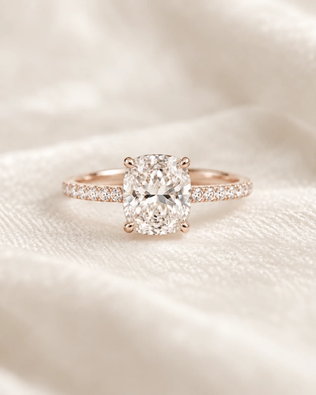 A cushion-cut diamond engagement ring with a pavé band in rose gold